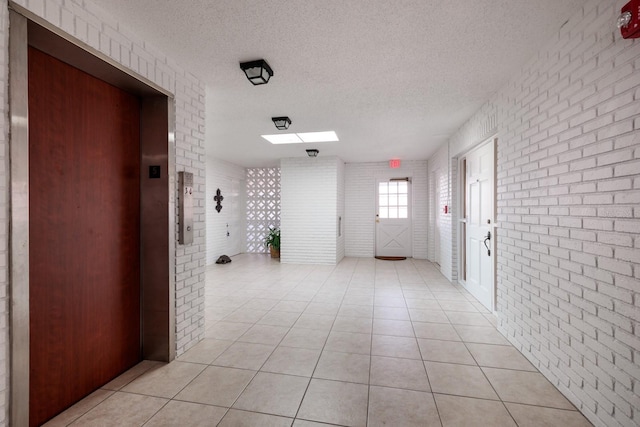 hallway featuring a textured ceiling, brick wall, elevator, and light tile patterned flooring