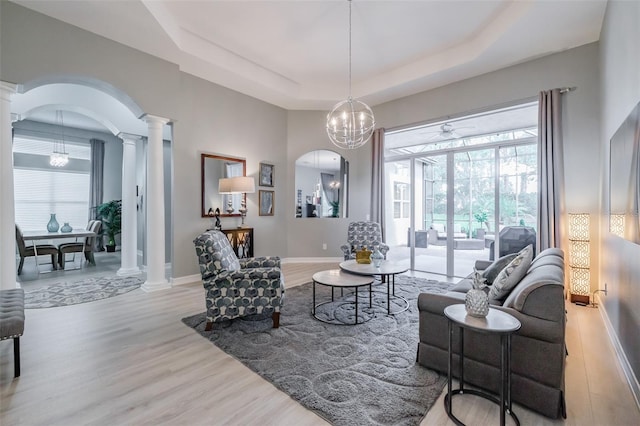 living room with a chandelier, a tray ceiling, and light wood-type flooring