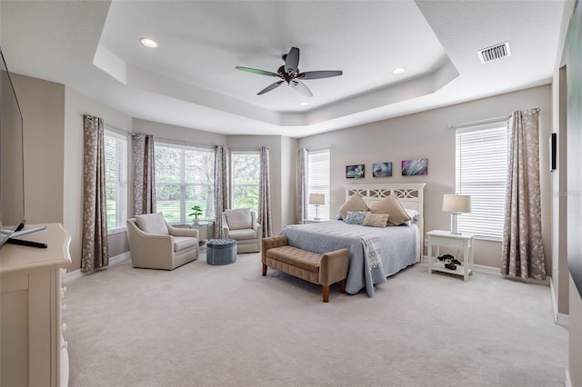 bedroom with ceiling fan, light colored carpet, and a raised ceiling