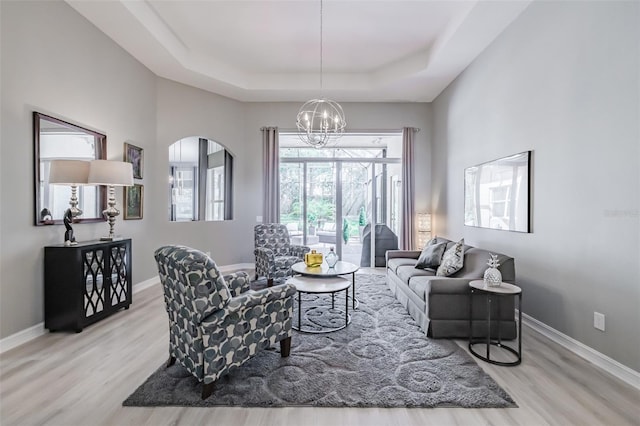 living room with a notable chandelier, light wood-type flooring, and a raised ceiling