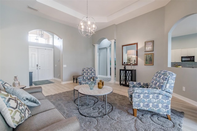 living room featuring a chandelier, a tray ceiling, light wood-type flooring, and decorative columns