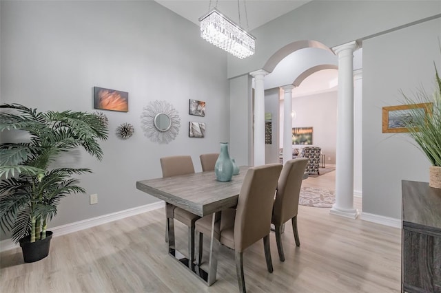 dining space with light hardwood / wood-style floors, an inviting chandelier, a towering ceiling, and decorative columns