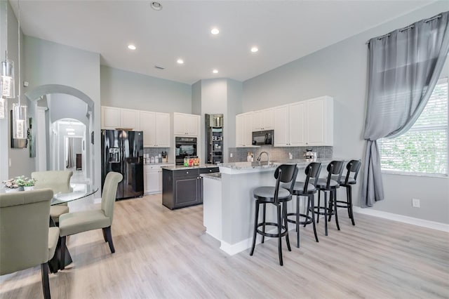 kitchen with light hardwood / wood-style flooring, white cabinets, black appliances, and an island with sink