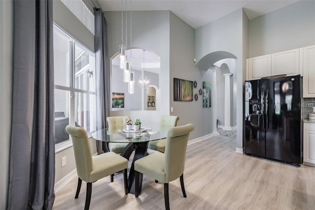 dining room with a towering ceiling, decorative columns, an inviting chandelier, and light hardwood / wood-style floors