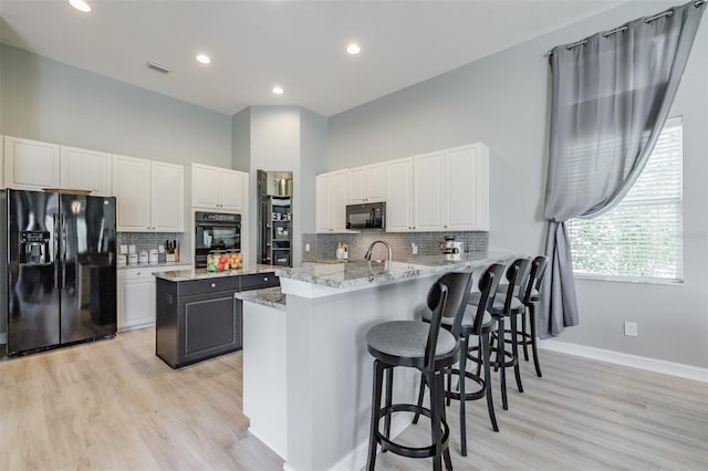 kitchen featuring black appliances, a kitchen island, white cabinets, light stone counters, and light hardwood / wood-style flooring