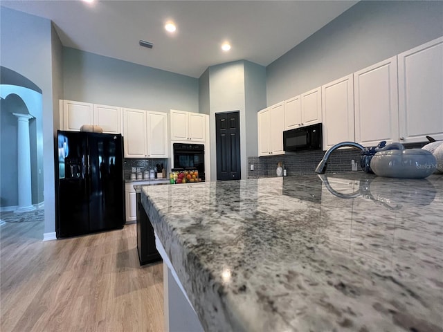 kitchen with white cabinets, backsplash, light stone countertops, black appliances, and a towering ceiling