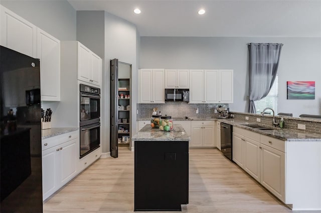 kitchen featuring white cabinetry, light wood-type flooring, black appliances, sink, and a center island