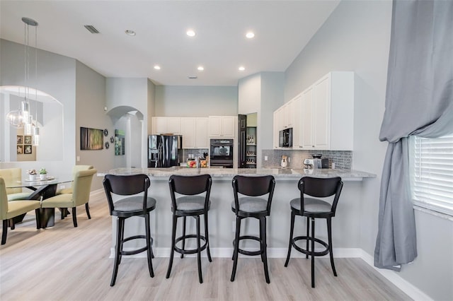 kitchen with kitchen peninsula, white cabinets, light wood-type flooring, black appliances, and decorative light fixtures