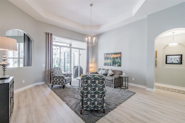 living room with an inviting chandelier, light wood-type flooring, and a raised ceiling