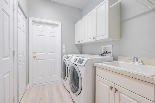 clothes washing area featuring cabinets, light hardwood / wood-style flooring, washer and dryer, and sink