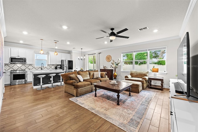 living room with sink, crown molding, light hardwood / wood-style floors, a textured ceiling, and ceiling fan with notable chandelier