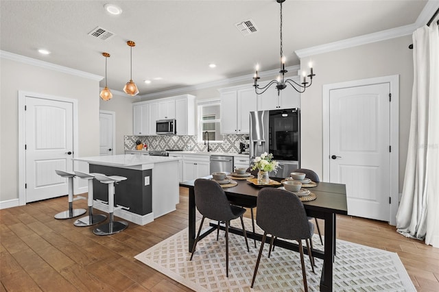 dining room featuring light hardwood / wood-style floors, an inviting chandelier, ornamental molding, and sink