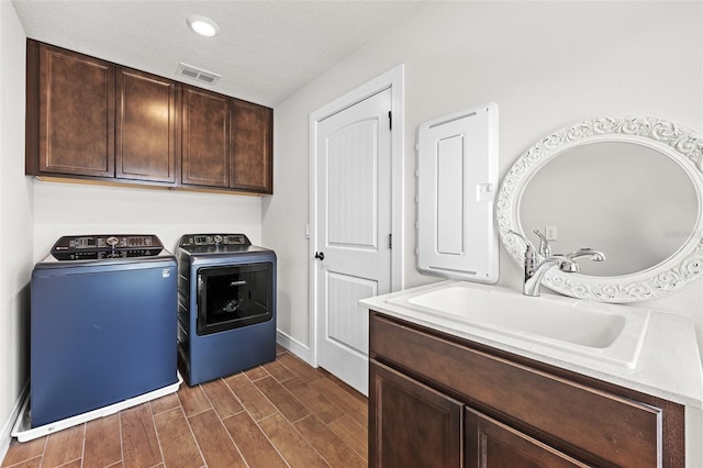 clothes washing area with cabinets, a textured ceiling, dark wood-type flooring, sink, and separate washer and dryer