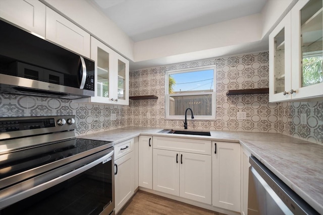 kitchen featuring appliances with stainless steel finishes, open shelves, a sink, and light countertops