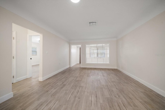 empty room featuring light wood finished floors, visible vents, and baseboards