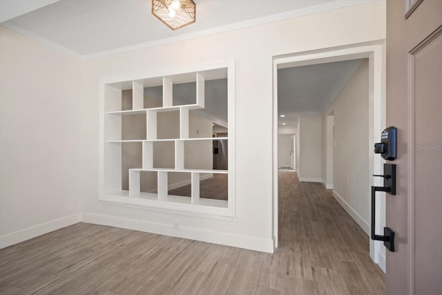 empty room featuring crown molding, wood finished floors, and baseboards