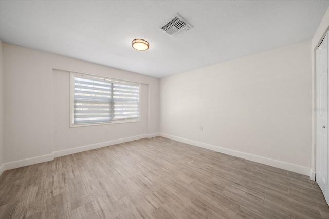 unfurnished room featuring light wood finished floors, visible vents, and baseboards