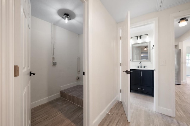 hallway featuring attic access, light wood-type flooring, a sink, and baseboards