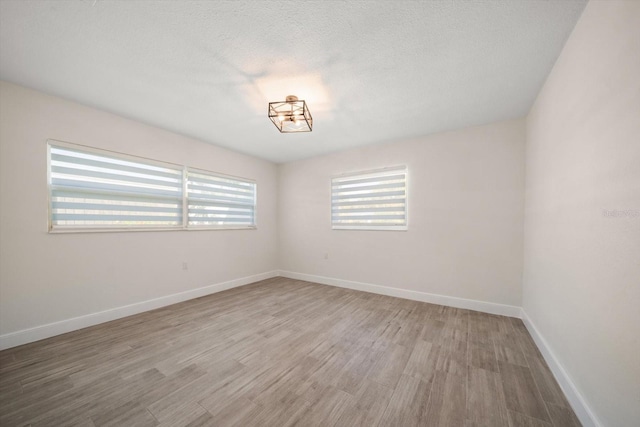 unfurnished room with baseboards, a textured ceiling, and light wood-style floors