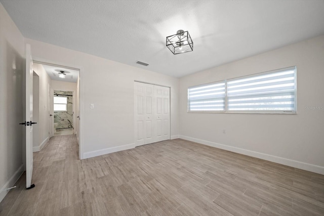 unfurnished bedroom with a closet, light wood-type flooring, visible vents, and baseboards