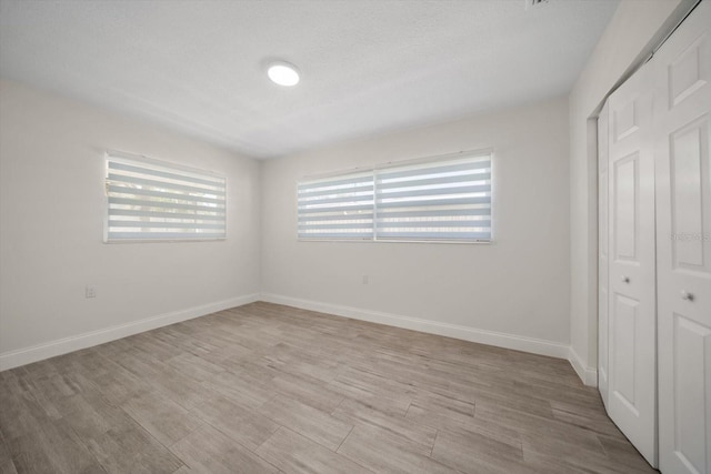 unfurnished bedroom with a closet, light wood finished floors, and baseboards