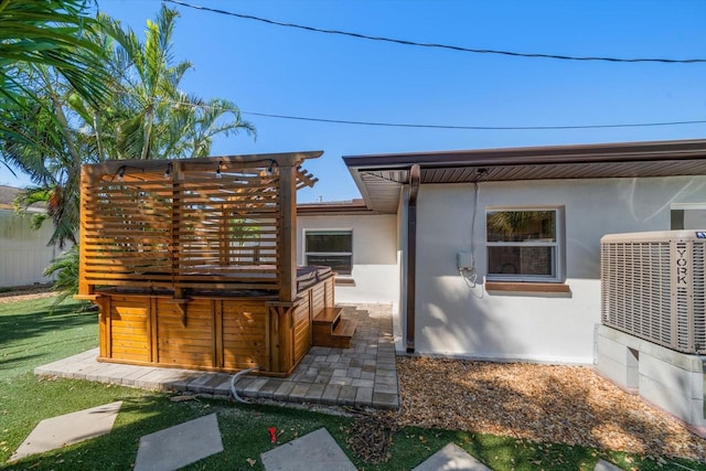 rear view of house featuring a hot tub, central AC unit, and stucco siding