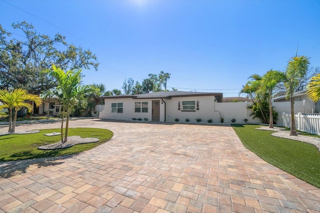 ranch-style home featuring a front lawn, decorative driveway, fence, and stucco siding