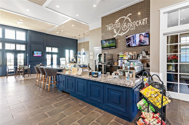 bar with decorative light fixtures, light stone countertops, blue cabinets, and a towering ceiling