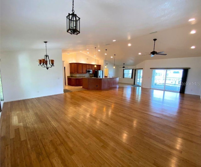 unfurnished living room featuring lofted ceiling, hardwood / wood-style floors, and ceiling fan with notable chandelier