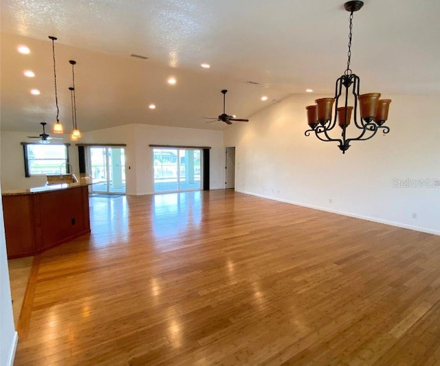 unfurnished living room featuring ceiling fan with notable chandelier, a healthy amount of sunlight, and hardwood / wood-style floors