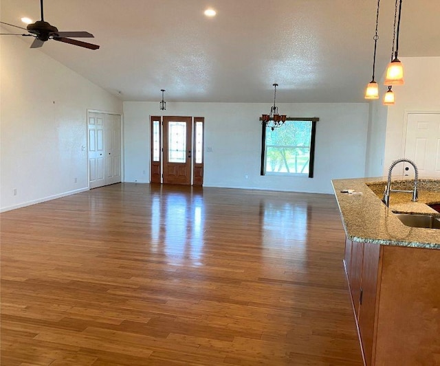 unfurnished living room featuring a healthy amount of sunlight, sink, ceiling fan with notable chandelier, and hardwood / wood-style flooring