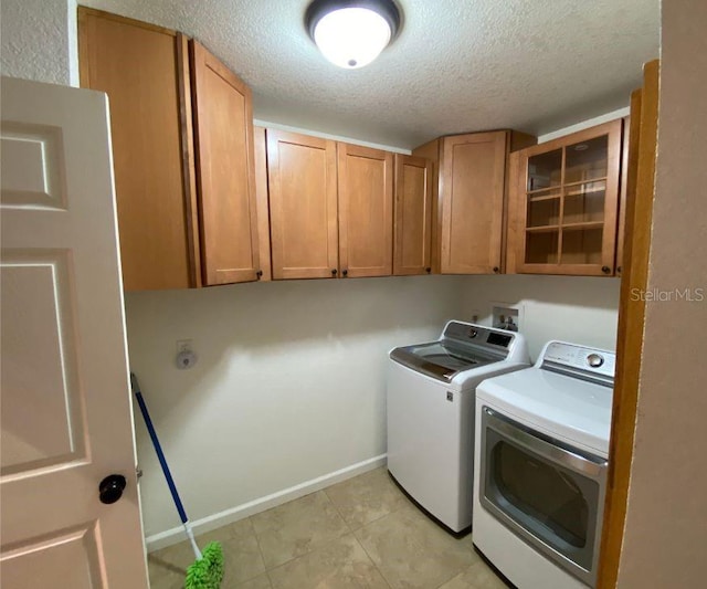 clothes washing area with light tile patterned floors, washing machine and clothes dryer, cabinets, and a textured ceiling