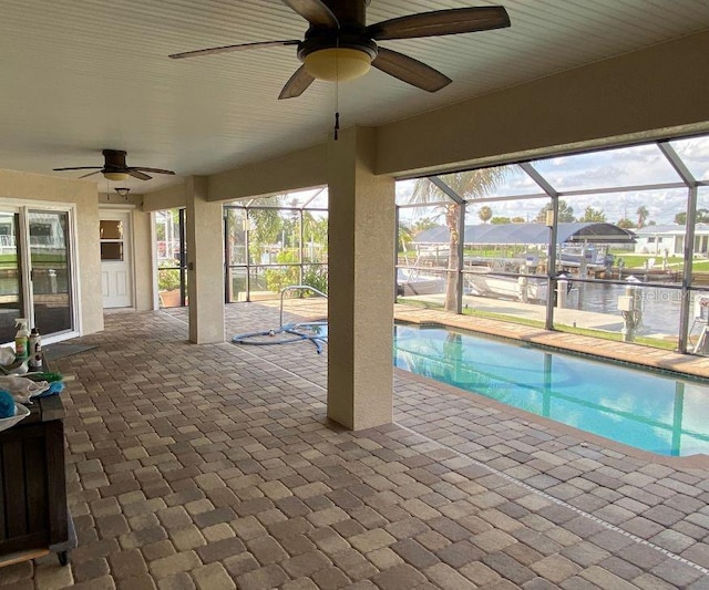 view of swimming pool featuring a lanai, ceiling fan, a patio, and a water view