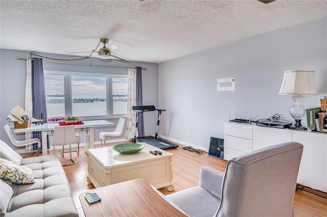 living room featuring a water view, ceiling fan, a textured ceiling, and light hardwood / wood-style flooring