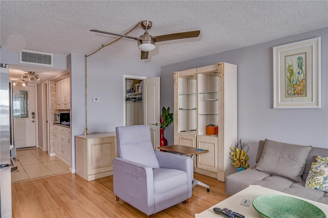 living room featuring light wood-type flooring, ceiling fan, and a textured ceiling