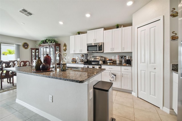 kitchen with light tile patterned floors, stainless steel appliances, sink, a center island with sink, and white cabinets