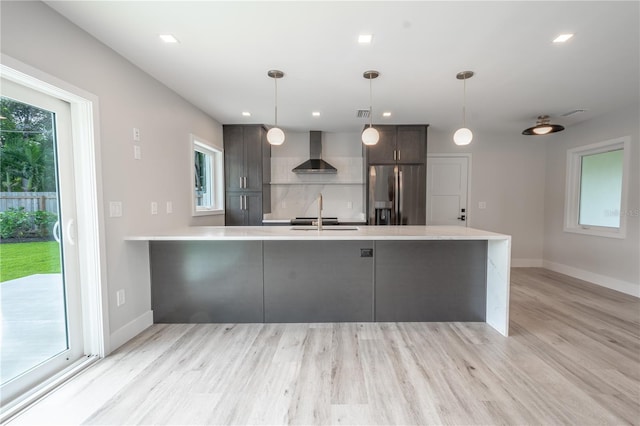 kitchen with wall chimney exhaust hood, stainless steel refrigerator with ice dispenser, light hardwood / wood-style floors, and hanging light fixtures