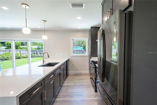 kitchen with appliances with stainless steel finishes, light stone countertops, pendant lighting, light hardwood / wood-style flooring, and sink