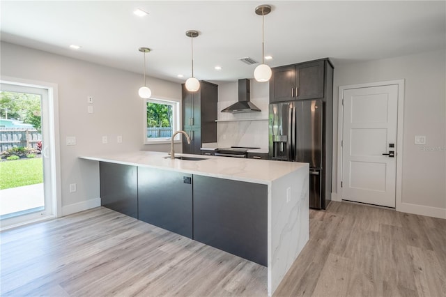 kitchen with appliances with stainless steel finishes, hanging light fixtures, kitchen peninsula, sink, and wall chimney range hood