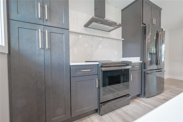 kitchen with wall chimney exhaust hood, decorative backsplash, appliances with stainless steel finishes, and light hardwood / wood-style flooring