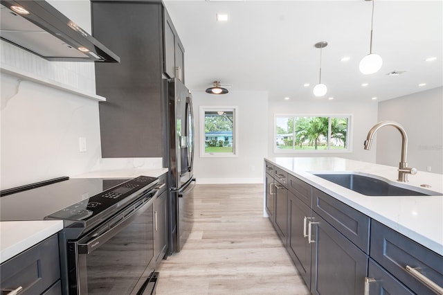 kitchen featuring sink, hanging light fixtures, wall chimney range hood, light hardwood / wood-style flooring, and stainless steel appliances