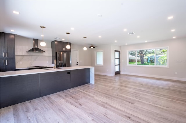 kitchen with hanging light fixtures, wall chimney exhaust hood, stainless steel fridge with ice dispenser, light wood-type flooring, and decorative backsplash