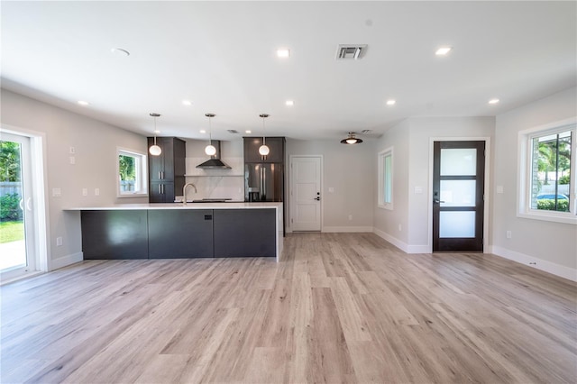 kitchen with hanging light fixtures, a healthy amount of sunlight, stainless steel fridge with ice dispenser, and wall chimney range hood