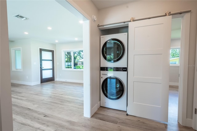 washroom with stacked washer and clothes dryer, a wealth of natural light, light hardwood / wood-style floors, and a barn door