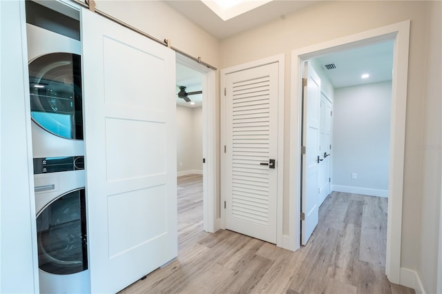 washroom with stacked washer / dryer, a barn door, and light hardwood / wood-style flooring