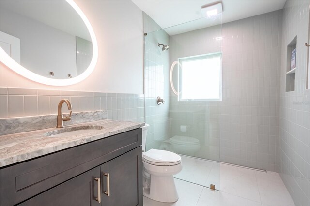 bathroom with tile walls, tiled shower, vanity, toilet, and tile patterned floors