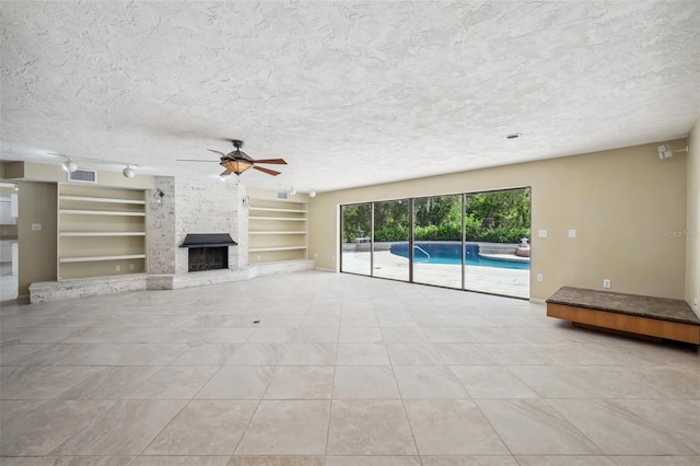 unfurnished living room with a textured ceiling, built in shelves, a large fireplace, and light tile patterned floors