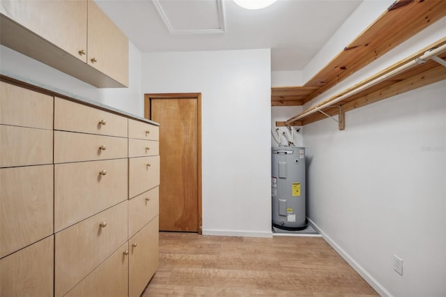 walk in closet with attic access, water heater, and light wood finished floors