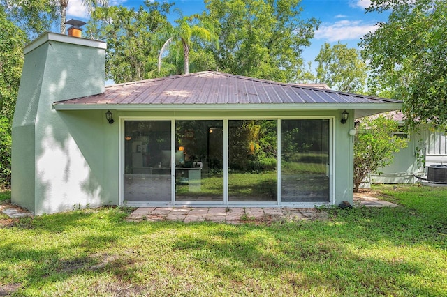 rear view of property featuring a lawn, a chimney, central AC, and metal roof