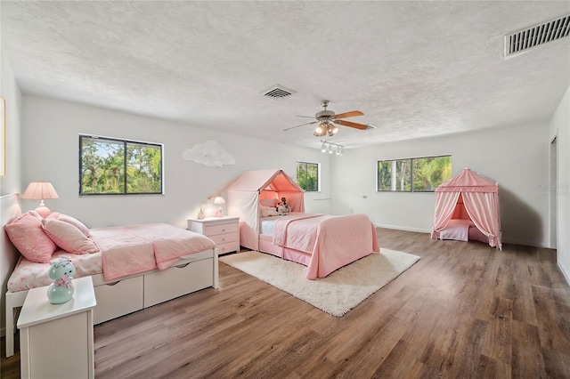 bedroom featuring a ceiling fan, wood finished floors, visible vents, and a textured ceiling